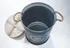 A dark gray metal laundry basket with rope handles and a wooden lid, shown from a slightly elevated side angle on a white background. Produktbild-Vorschau