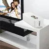 A white cable management box is placed on a white table next to a television displaying a couple on a beach. Náhľad obrázku produktu
