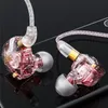 Close-up studio shot of two in-ear headphones with transparent pink casings, resting on a dark reflective surface. Produktbild-Vorschau