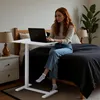A woman is working on her laptop while sitting on a bed, with a mobile desk next to her. Voir les images du produit