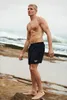 A man standing on a rocky beach with waves in the background. Produktbild-Vorschau