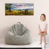 A young child stands next to a large gray beanbag chair in a room with a painting on the wall. Produktbild-Vorschau