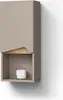 A modern, wall-mounted bathroom cabinet with a door and an open shelf, displaying a candle. Produktbild-Vorschau