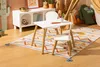 A child's play area with a white table and chairs set on a colorful rug, next to a storage unit and a teepee. Náhled obrázku produktu