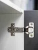 A close-up view of a cabinet hinge connecting a white cabinet door to a dark gray cabinet frame. Produktbild-Vorschau