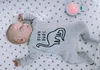 A baby sleeping in a crib with a star-patterned sheet, wearing a onesie with a dinosaur graphic and the text 'DINO DUDE'. A small, round, pink night light is visible in the upper right corner. Produktbild-Vorschau