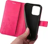 A hand holding a pink flip phone case with a floral and butterfly embossed design, revealing the black interior where a phone would be placed. Produktbild-Vorschau