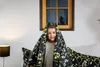 A young girl is peeking out from under a black and gold floral patterned duvet in a bedroom setting. Podgląd zdjęcia produktu