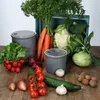 A collection of fresh vegetables and two gray storage containers arranged on a wooden surface. Produktbild-Vorschau