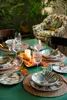 A table setting with tropical-themed tableware, candles, and autumn leaves, suggesting a festive or decorative arrangement. Produktbild-Vorschau