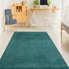 A teal rug is laid out on a light-colored floor in a room with a wooden cabinet, a desk with a computer, and chairs. Produktbild-Vorschau
