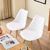 Two white chairs with wooden legs are placed in a room with a wooden table in the foreground. A book and a cup are on the table. Voir les images du produit