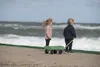 Two children stand on a beach with a green wagon, looking out at the ocean. Produktbild-Vorschau