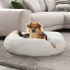 A dog is resting in a fluffy white dog bed on a gray rug in front of a sectional sofa. Podgląd zdjęcia produktu