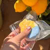 A hand holding a star-shaped clear plastic package containing a yellow and blue resin art piece, with lemons in the background. Voir les images du produit