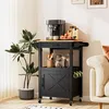 A black kitchen cart with a wooden top is set up as a coffee station next to a sofa and a large potted plant. Podgląd zdjęcia produktu