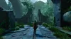 A person walks down a stone path towards ancient ruins overgrown with vegetation. Produktbild-Vorschau