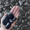 Schwarze polierte Kieselsteine auf einer Handfläche zur Größendarstellung Produktbild-Vorschau