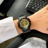 A person wearing a black and gold Casio G-shock watch on their wrist, with a keyboard in the background. Anteprima dell’immagine prodotto