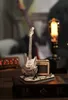 A miniature wooden electric guitar and amplifier model is displayed on top of a stack of books, with a vintage-style lamp in the background. Voir les images du produit