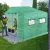 A man is holding a plant in front of a green greenhouse in a garden setting. Voir les images du produit