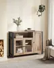 A wooden sideboard with glass doors and black metal legs, placed in a living room setting with a fireplace and a hanging plant. Náhled obrázku produktu
