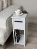 A white bedside table with a drawer and shelf, placed next to a textured sofa. Náhľad obrázku produktu
