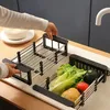 A person is adjusting an adjustable sink rack filled with vegetables in a kitchen sink. Produktbild-Vorschau