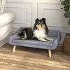 A dog is lying on a gray pet sofa with wooden legs, placed on a wooden floor next to a couch and a plant. Produktbild-Vorschau