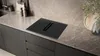 A modern kitchen countertop with a black induction hob and integrated extractor fan. Produktbild-Vorschau
