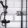 A black shower shelf is attached to a glass shower door, next to a black shower fixture and shower head on a tiled wall. Náhled obrázku produktu