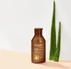 A bottle of Redken All Soft Mega Curls Shampoo is placed next to two aloe vera plants against a light-colored wall and a peach-colored surface. Produktbild-Vorschau