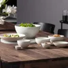 A collection of white ceramic bowls of various sizes are arranged on a wooden table, with a salad in the largest bowl and grilled vegetables in a shallow bowl. Podgląd zdjęcia produktu
