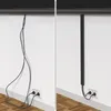 A split image showing a messy tangle of black cables on the left and the same cables neatly organized within a black cable channel on the right, next to a white wall with electrical outlets. Anteprima dell’immagine prodotto
