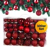 A set of red Christmas ornaments in a clear plastic box, with a festive green garland in the background. Náhled obrázku produktu