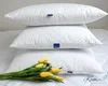 Three white pillows are stacked on a bed, with a bouquet of yellow tulips in front of the bottom pillow. Produktbild-Vorschau