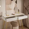 A white vanity table with gold legs and open drawers, decorated with a bust, makeup brushes, and a mirror. A stool is placed in front of the table. Produktbild-Vorschau