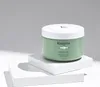 A green jar of hair product sits on white pedestals against a light gray background. Produktbild-Vorschau