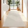A long, beige runner rug is laid out in a hallway with wooden floors. Two potted plants are visible near a large window at the end of the hallway. Anteprima dell’immagine prodotto