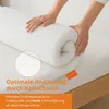 Hands are shown rolling up a white mattress topper on a bed. Náhľad obrázku produktu