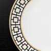 A close-up view of the rim of a white plate with a black and gold geometric pattern. Náhled obrázku produktu