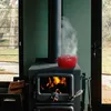 A red cast iron humidifier is placed on top of a wood-burning stove, with steam rising from it. Podgląd zdjęcia produktu