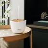 A white and gold aroma diffuser sits on a round tan tray, emitting a thin stream of vapor. White orchid flowers are visible in the background. Produktbild-Vorschau