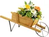 A wooden wheelbarrow planter filled with colorful flowers and greenery, set against a white background. Podgląd zdjęcia produktu