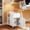 A white mobile cabinet with drawers and doors, placed next to a desk in a room with a yellow wall and a rug. Náhľad obrázku produktu
