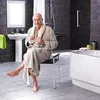 An elderly man sits on a stool in a modern bathroom, wearing a bathrobe and holding a towel. Produktbild-Vorschau