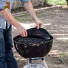 A person is placing a round, black grill mat onto a charcoal grill. Produktbild-Vorschau