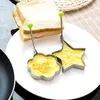Two metal egg molds, one star-shaped and one flower-shaped, are on a white plate. Each mold contains a cooked egg. Slices of white bread are in the background. Produktbild-Vorschau