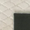 A close-up view of a cream-colored rug with a diamond-patterned texture and a black backing with white dots. Anteprima dell’immagine prodotto