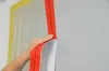 A hand is shown applying a red zipper to a wall, which is partially covered by a white sheet. Yellow tape is visible in the background. Produktbild-Vorschau